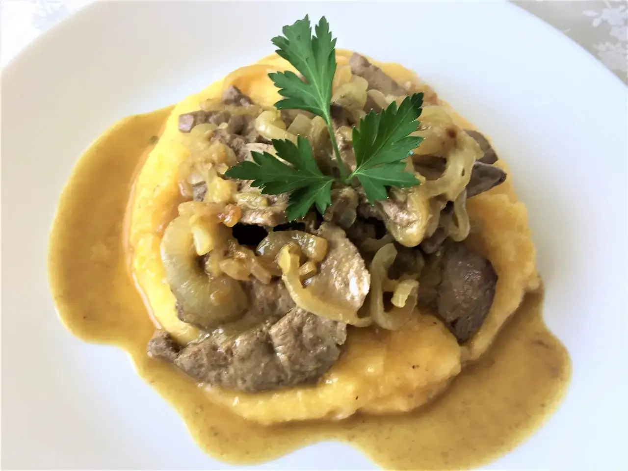 Piatto di fegato alla veneziana con cipolle e polenta morbida, guarnito con prezzemolo fresco.