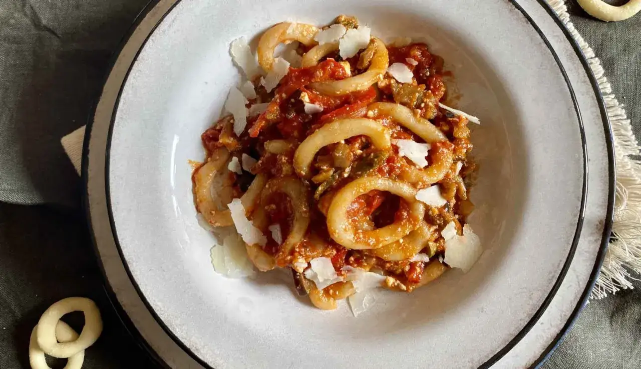 Un piatto di anellini alla pecorara, pasta a forma di anello condita con sugo di pomodoro, verdure e scaglie di formaggio.