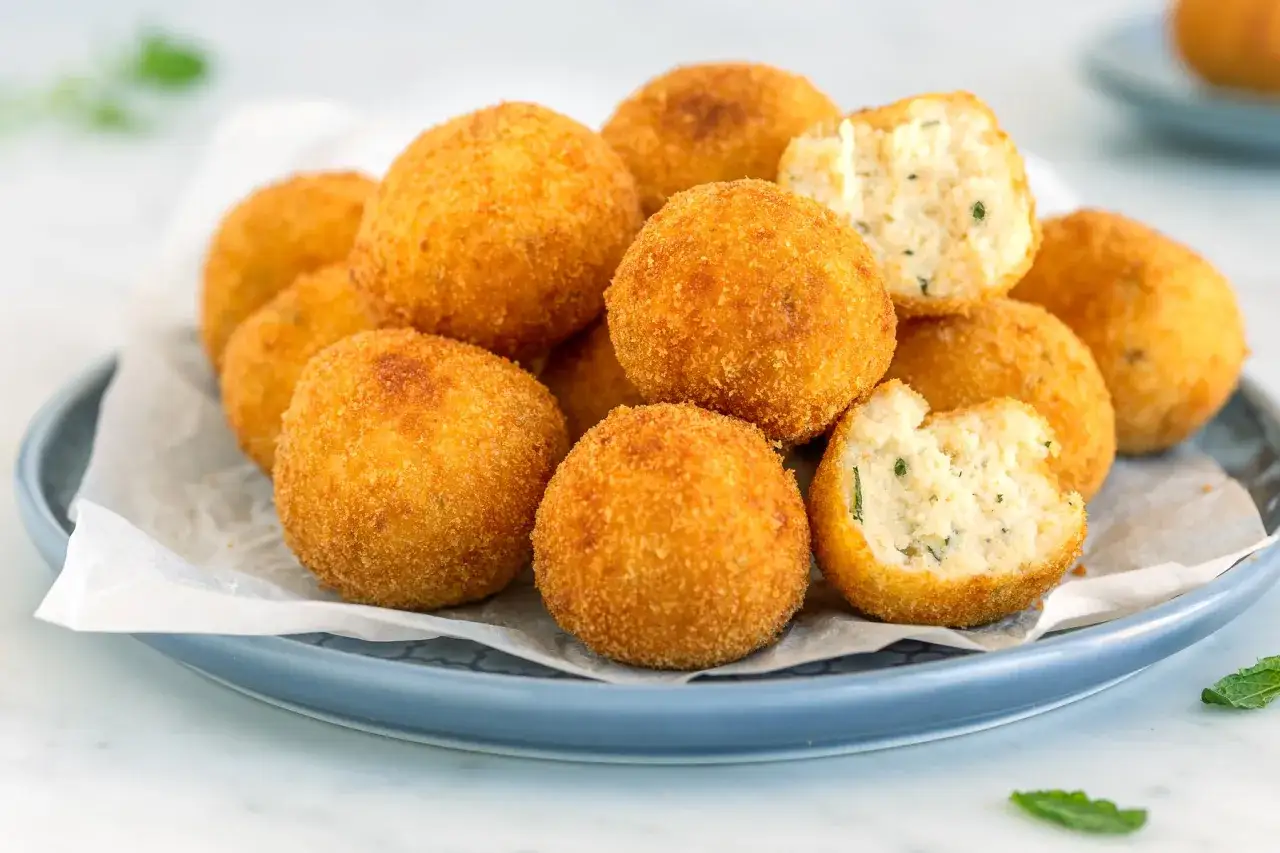 Un mucchio di polpette di ricotta dorate e croccanti, alcune delle quali sono state morse rivelando un interno morbido e saporito.