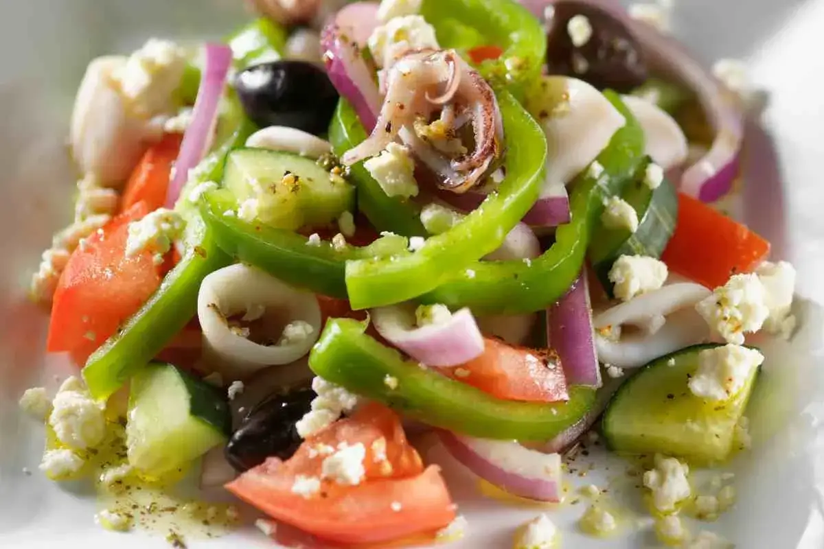 Insalata di calamari fresca con pomodori, cetrioli, peperoni verdi, cipolla rossa, olive nere e formaggio feta.