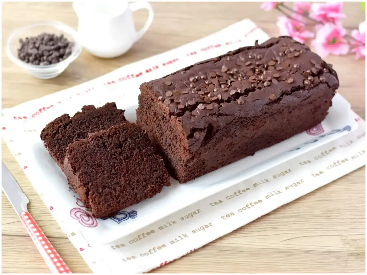 Un delizioso plumcake al cioccolato, cosparso di gocce, &egrave; affettato su un piatto. Accanto, una ciotola di gocce e una brocca di latte.