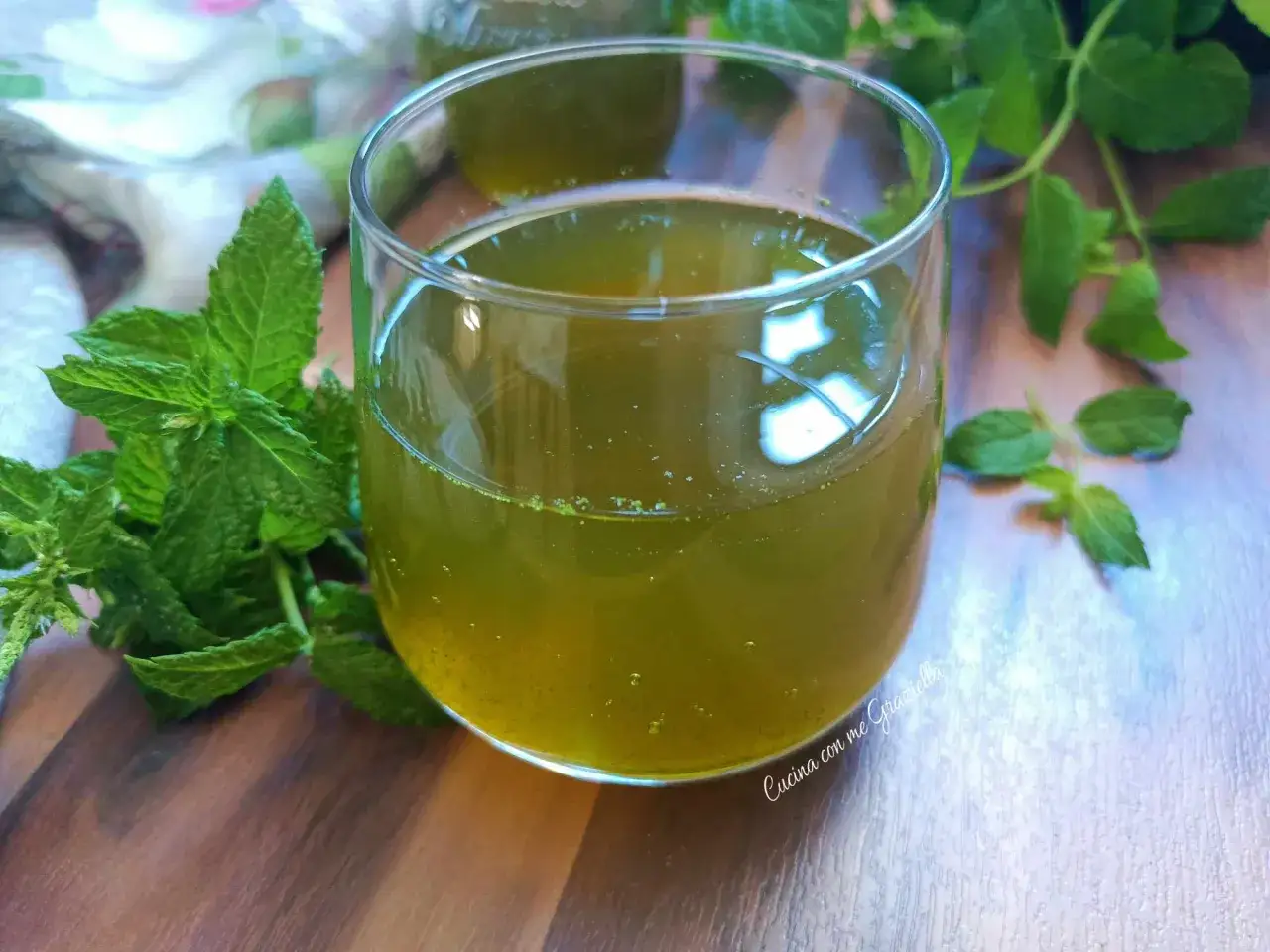 Un bicchiere di sciroppo di menta, rinfrescante e profumato, con foglie di menta fresca su un tavolo di legno.