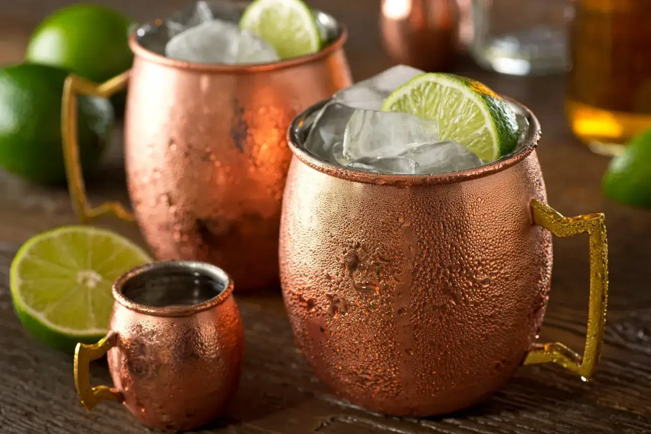 Coppe di rame con ghiaccio, lime e una piccola tazza, perfetti per la moscow mule ricetta.