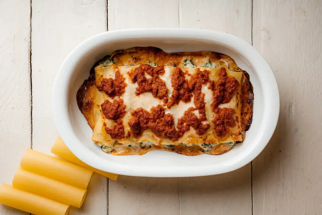 Cannelloni ricotta e spinaci appena sfornati, dorati e ricoperti di sugo rosso, pronti per essere gustati.