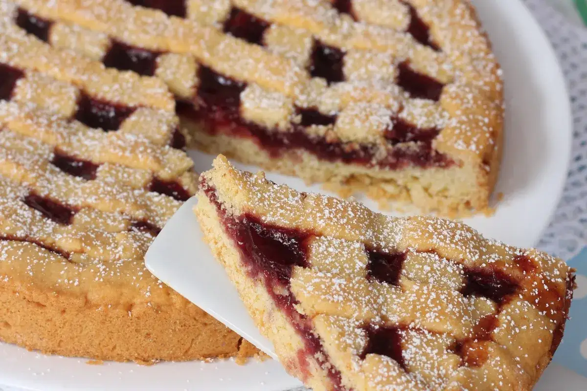 Deliziosa crostata senza burro con marmellata di ciliegie, cosparsa di zucchero a velo. Una fetta è servita su una paletta.
