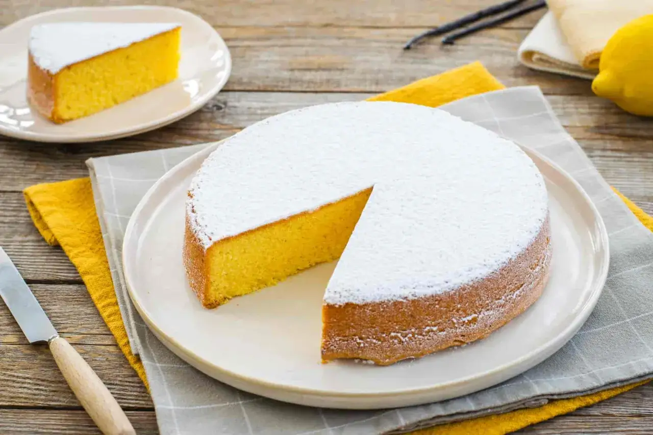 Una torta paradiso soffice e dorata, spolverata di zucchero a velo. Una fetta &egrave; gi&agrave; servita, pronta per essere gustata. La ricetta perfetta per un dolce semplice e delizioso.