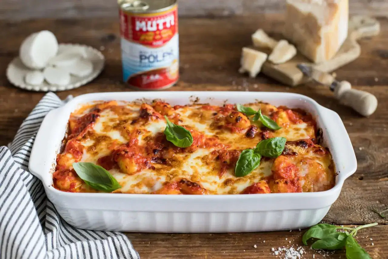 Gnocchi alla sorrentina appena sfornati, filanti e dorati, con pomodoro e basilico fresco. Accanto, mozzarella, parmigiano e una lattina di polpa Mutti.
