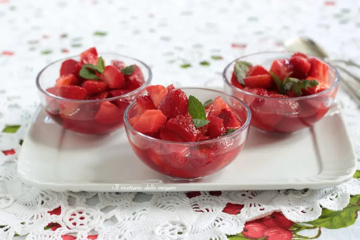Tre coppette di macedonia di frutta con fragole fresche e menta, servite su un vassoio bianco.