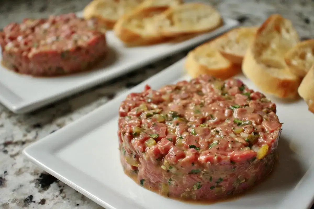 Tartare di manzo come condirla: un piatto raffinato con carne cruda, capperi, cipolla e prezzemolo, servito con crostini.