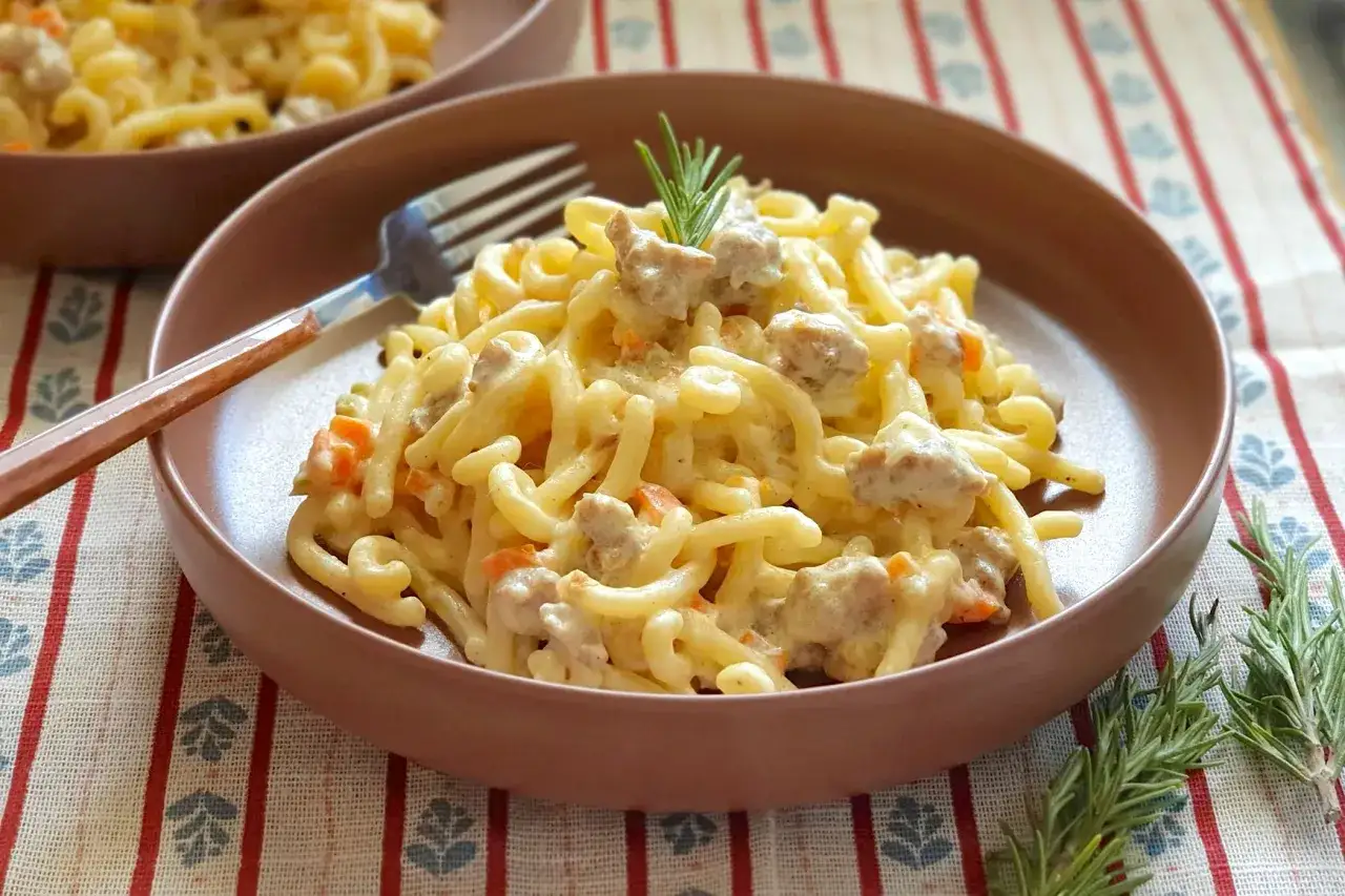 Gramigna alla salsiccia cremosa, con pezzetti di salsiccia e carote, guarnita con rosmarino fresco. Un piatto invitante.