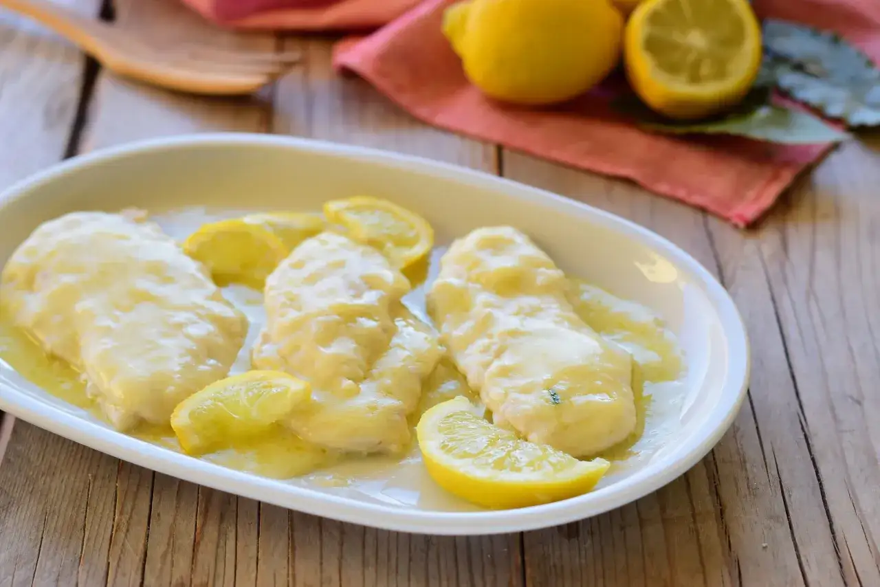 Scaloppine al limone cremose, servite su un piatto bianco con fette di limone fresco.