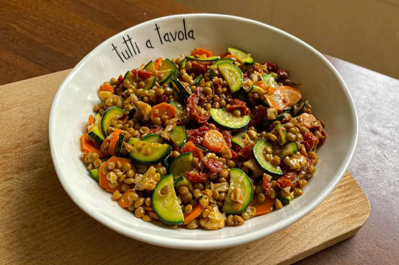 Un'appetitosa insalata di lenticchie estiva con zucchine, carote e pomodori secchi, servita in una ciotola con la scritta