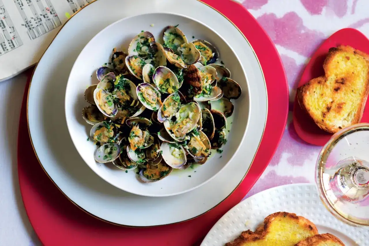 Un invitante sautè di vongole, condito con prezzemolo fresco e aglio, servito con crostini dorati e un bicchiere di vino bianco.