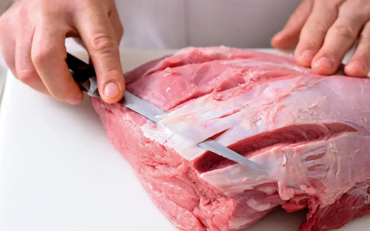 Mani esperte preparano un succulento arrosto di vitello, incidendo la carne con un coltello affilato per una cottura perfetta.