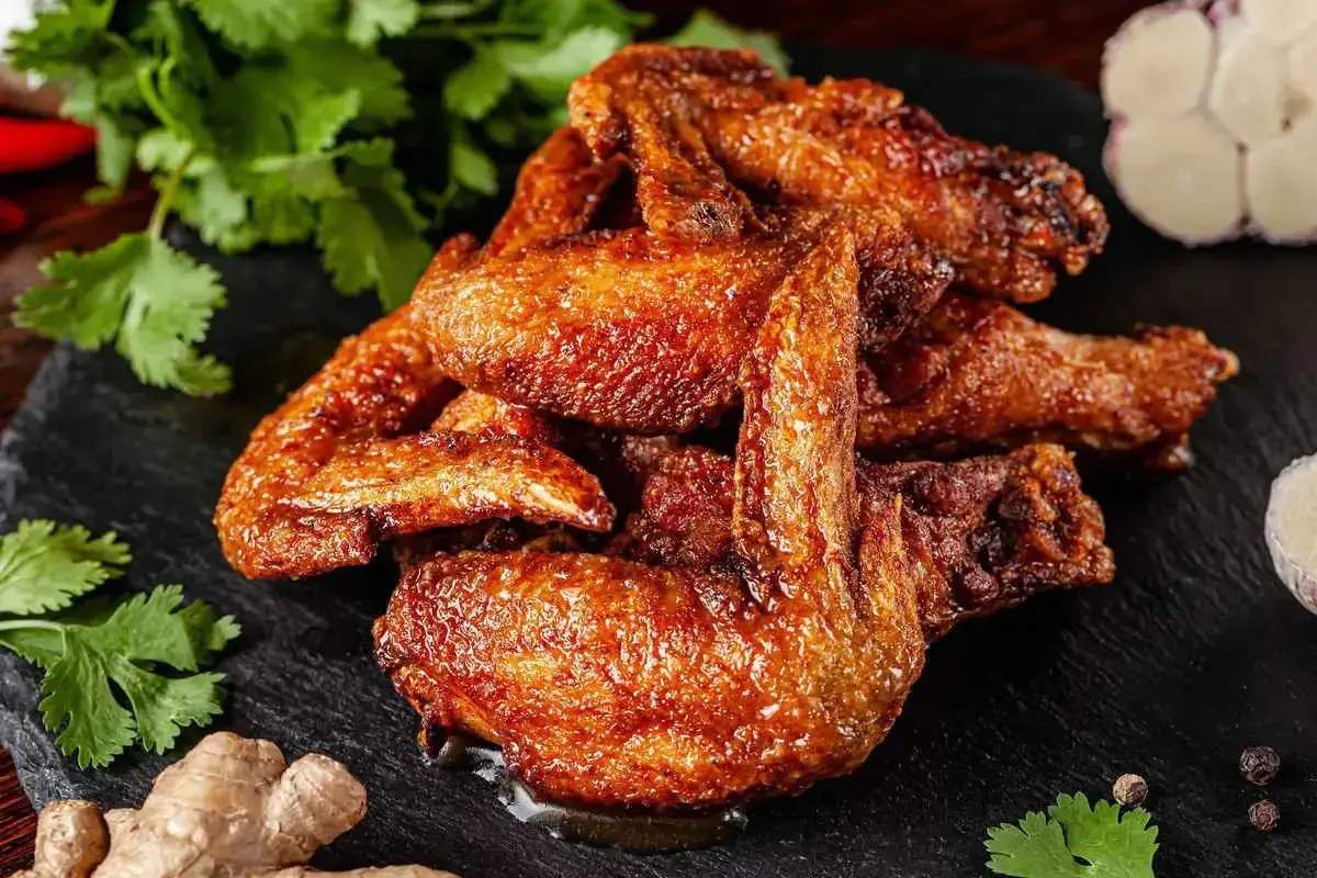 Alette di pollo al forno dorate e succulente, servite su una pietra scura con coriandolo fresco, zenzero e aglio.