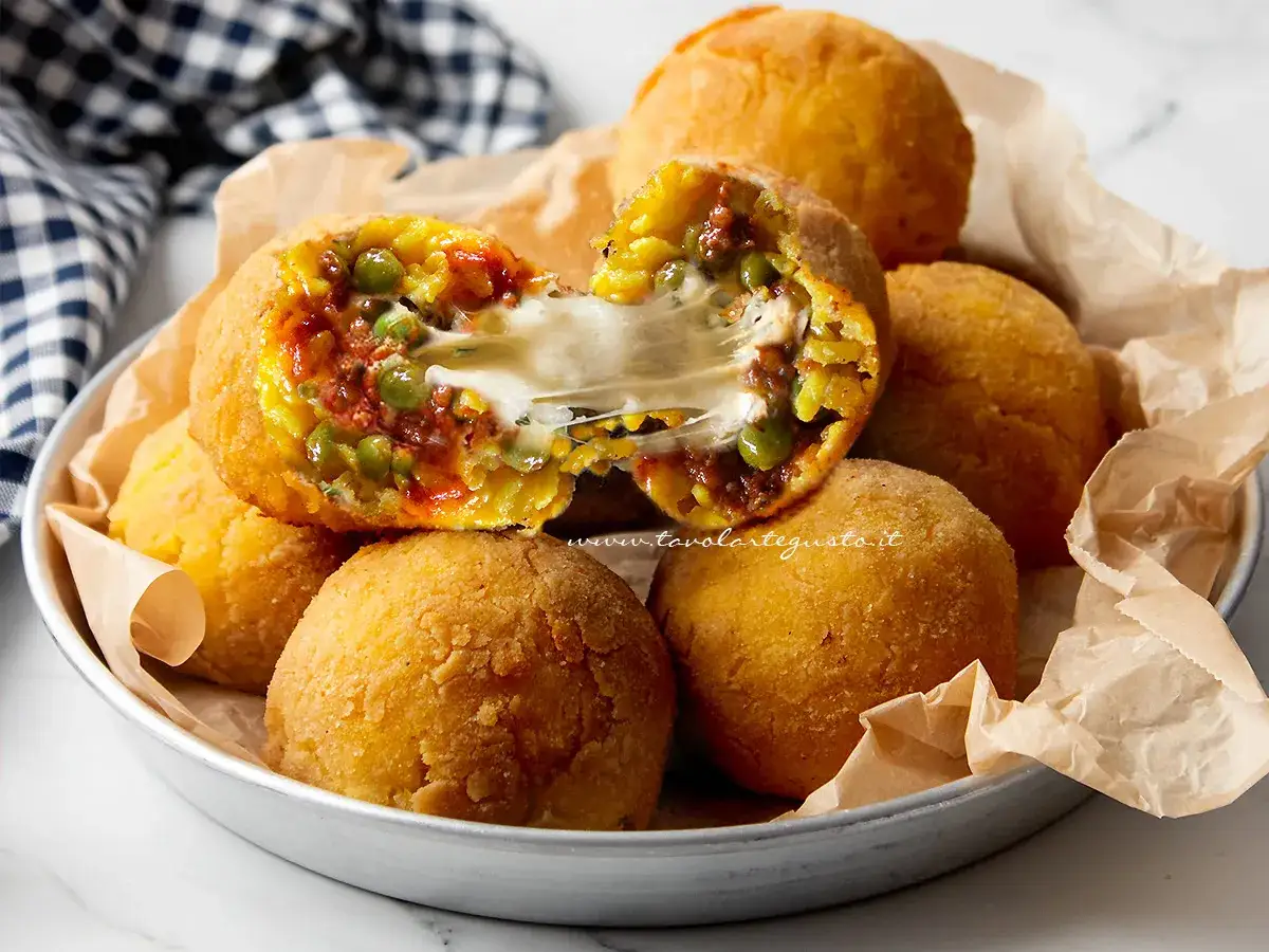 Arancini di riso dorati e croccanti, uno aperto rivela un cuore filante di formaggio, piselli e ragù.