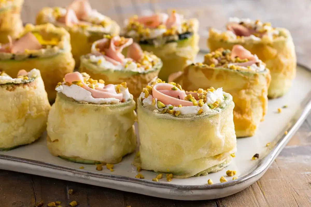 Rotolini di zucchine fritte con crema, prosciutto e pistacchi: stuzzichini veloci ed economici per aperitivo.