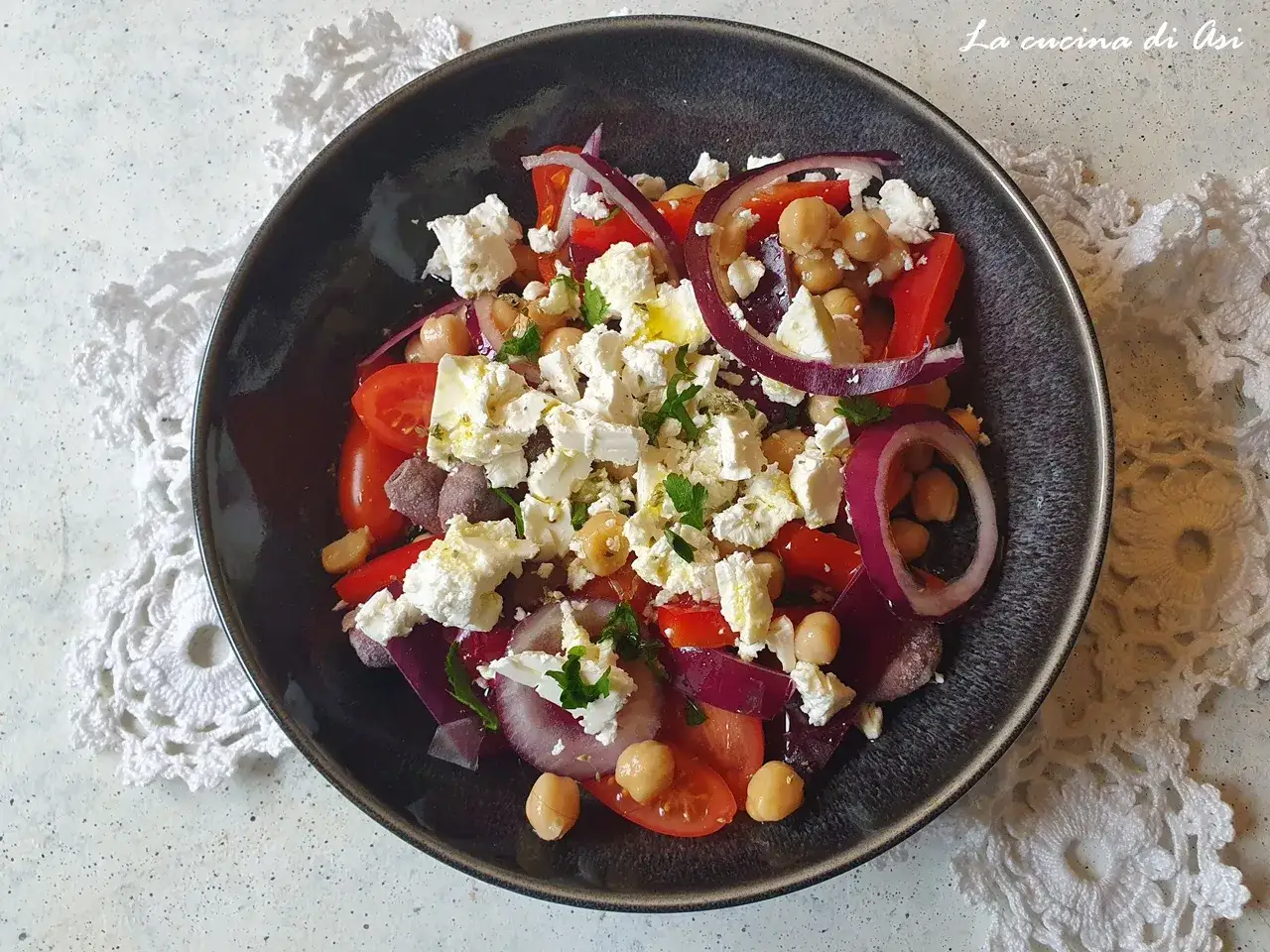 Insalata di ceci colorata con pomodori, cipolla rossa, feta e olive nere, condita con erbe aromatiche.