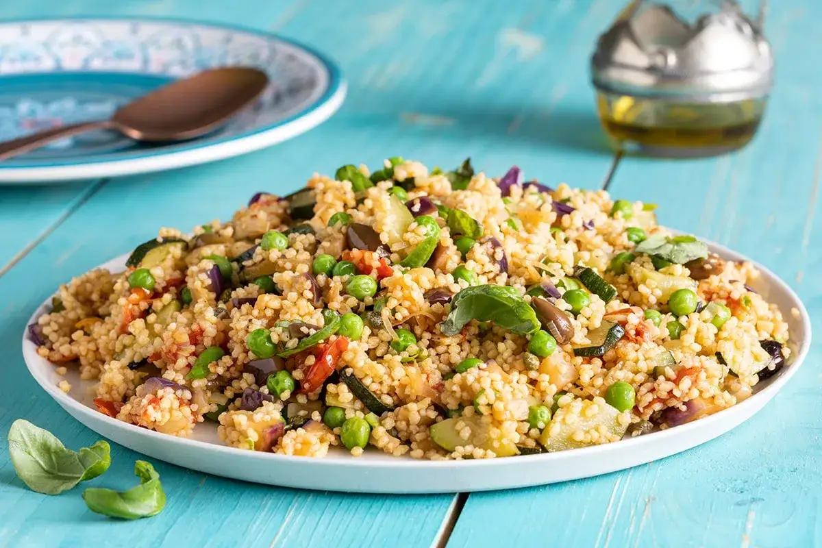 Un piatto colorato di cous cous con verdure miste, piselli e basilico fresco. Una ricetta cous cous leggera e gustosa.