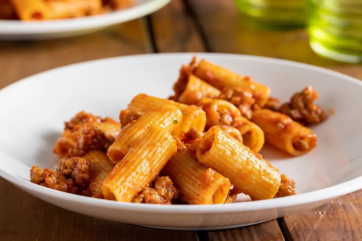 Rigatoni conditi con un ricco rag&ugrave; di salsiccia, serviti su un piatto bianco.