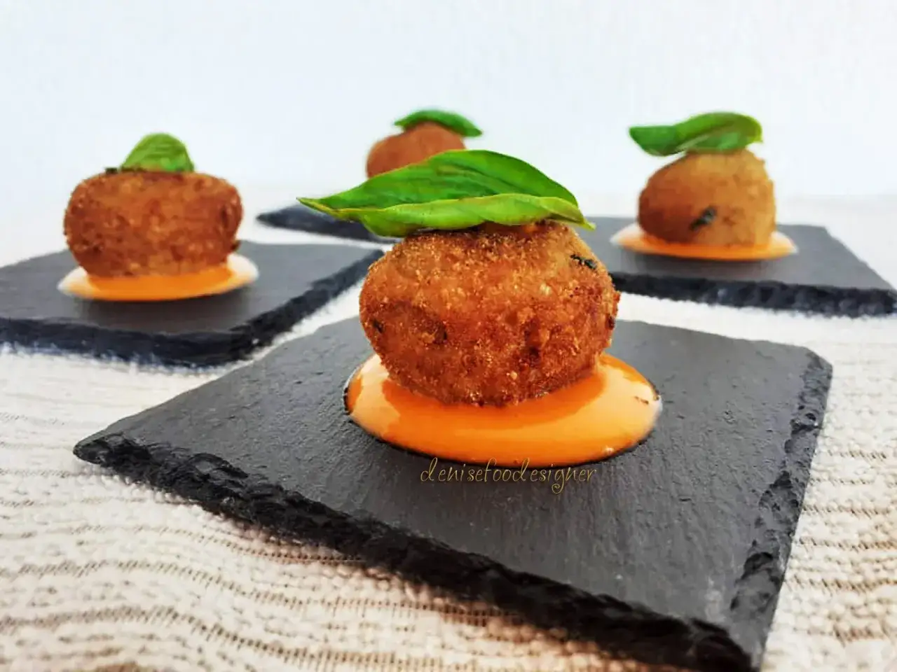 Deliziose polpette di melanzane fritte, servite su ardesia con salsa arancione e basilico fresco.