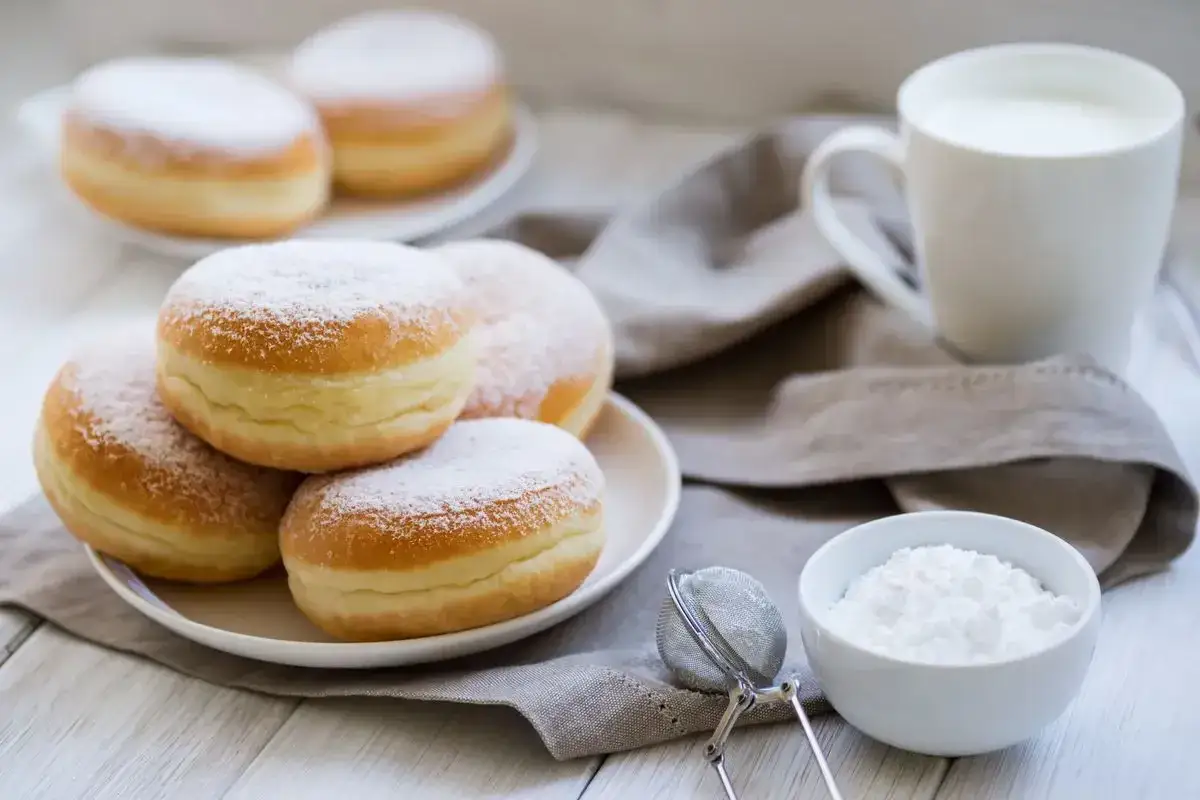 Bomboloni alla crema spolverati di zucchero a velo, pronti per essere gustati con un bicchiere di latte.