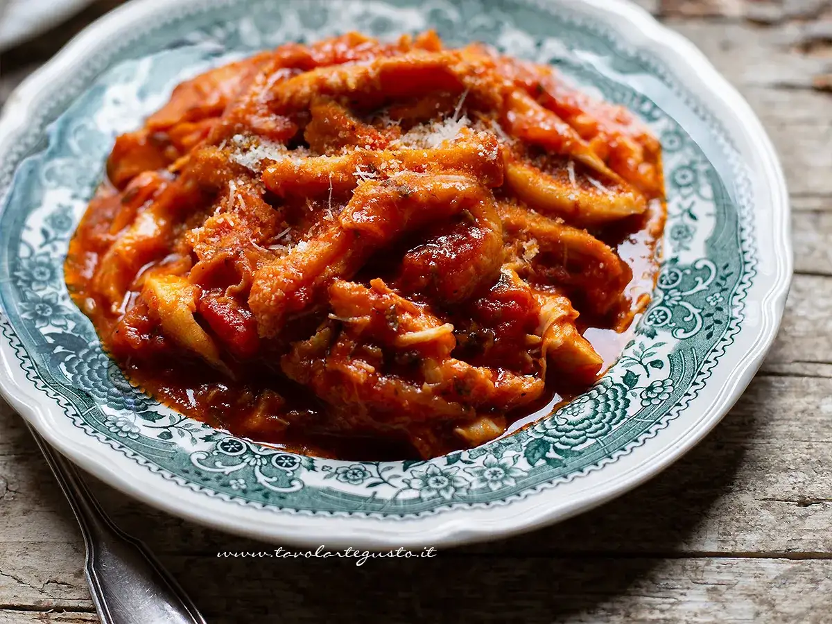 Trippa alla romana, la ricetta della nonna, servita su un piatto decorato con un sugo rosso e formaggio grattugiato.