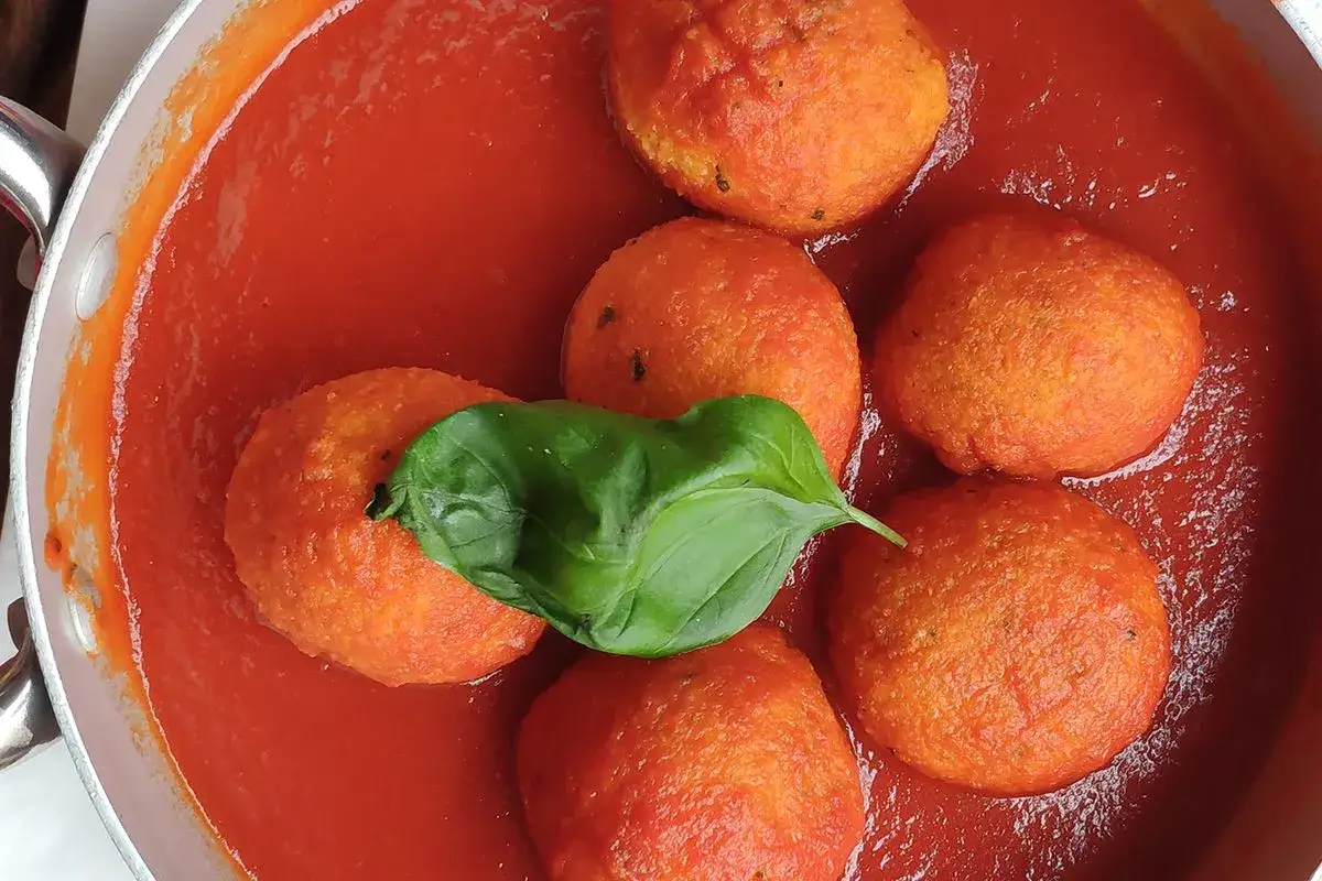 Pallotte cacio e ova in un sugo rosso, guarnite con una foglia di basilico fresco.