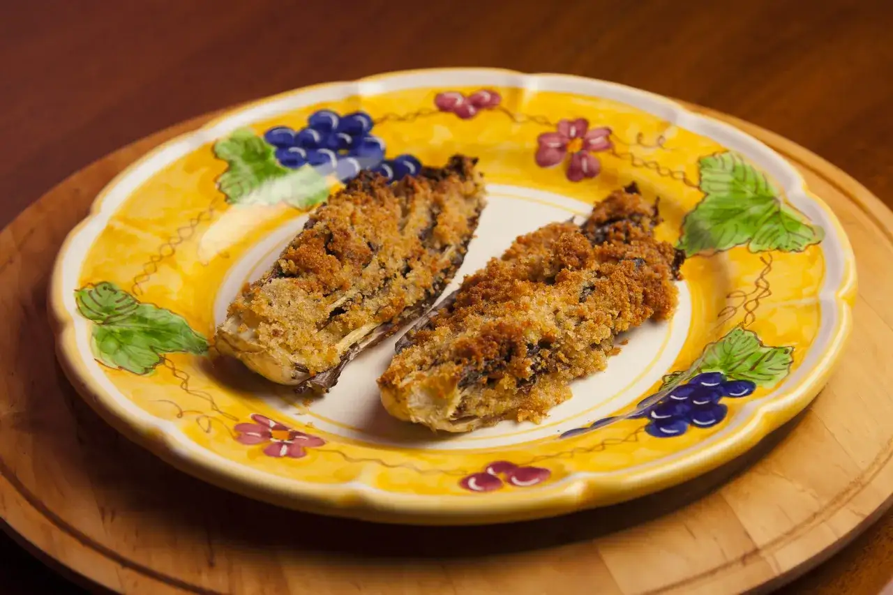 Due metà di radicchio al forno, dorate e croccanti, servite su un piatto giallo decorato con uva e fiori.
