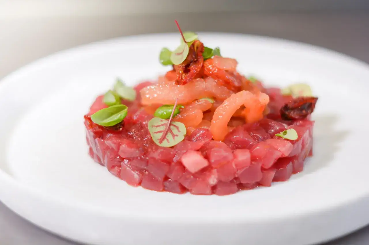 Deliziosa tartare di tonno, fresca e colorata, guarnita con pomodori secchi e germogli verdi.