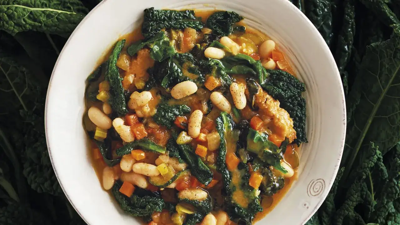 Una ciotola di zuppa di cavolo nero, ricca di fagioli cannellini, carote e sedano, con foglie di cavolo nero che spuntano.