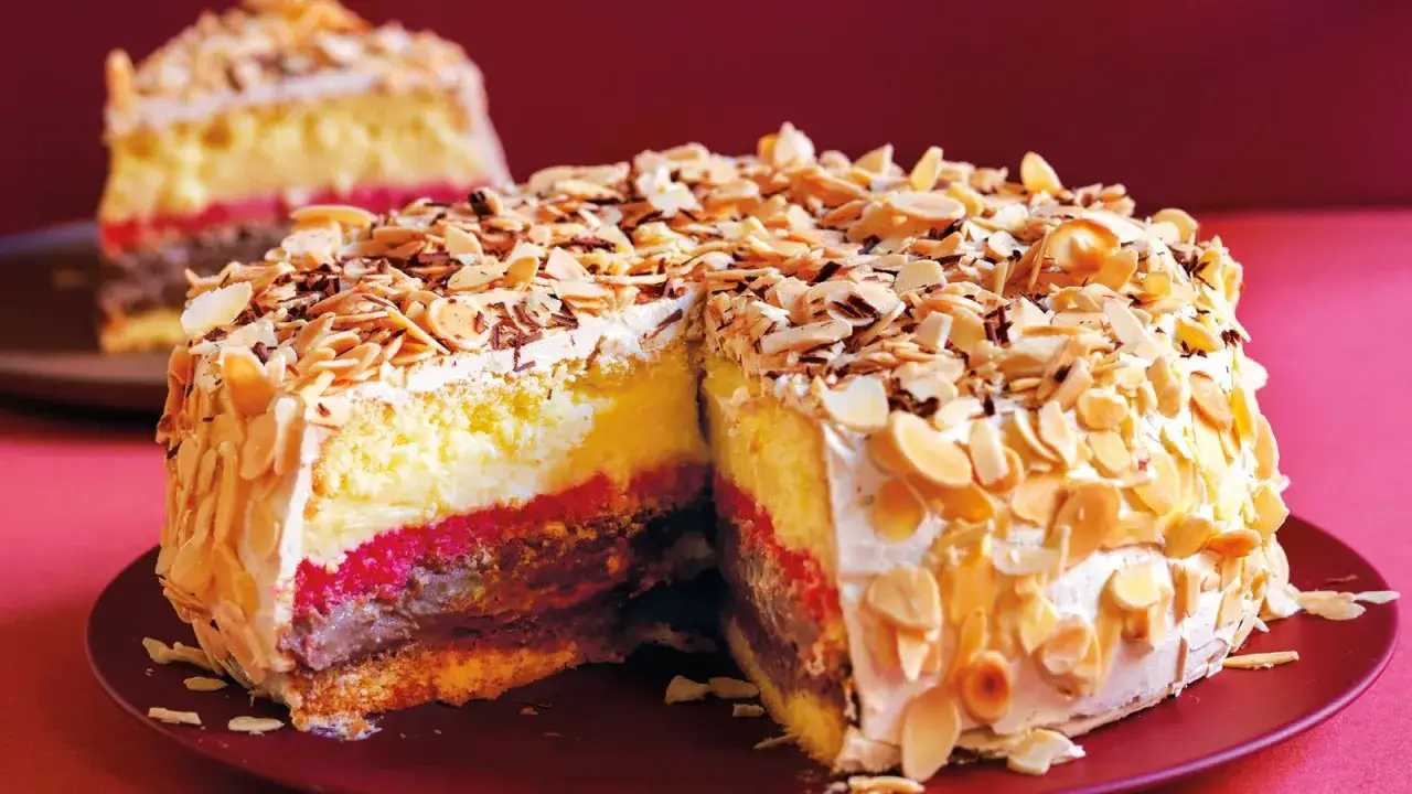 Una fetta di pizza dolce abruzzese, con strati di crema, marmellata e cioccolato, ricoperta di mandorle tostate e meringa.