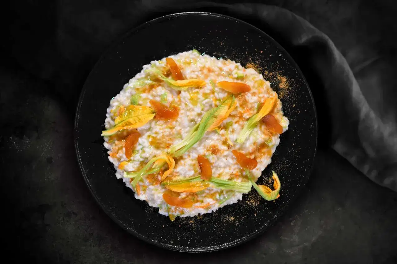 Risotto ai fiori di zucca cremoso, guarnito con petali freschi e un tocco di polvere dorata.