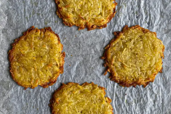 Quattro rosti di patate dorati e croccanti su carta da forno.