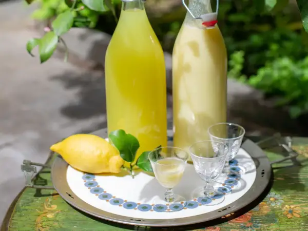 Due bottiglie di limoncello, una chiara e una cremosa, con limone fresco e bicchierini pronti per un assaggio.