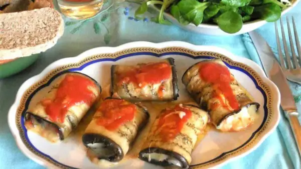 Deliziosi involtini di melanzane ripieni, conditi con sugo di pomodoro, su un piatto decorato.